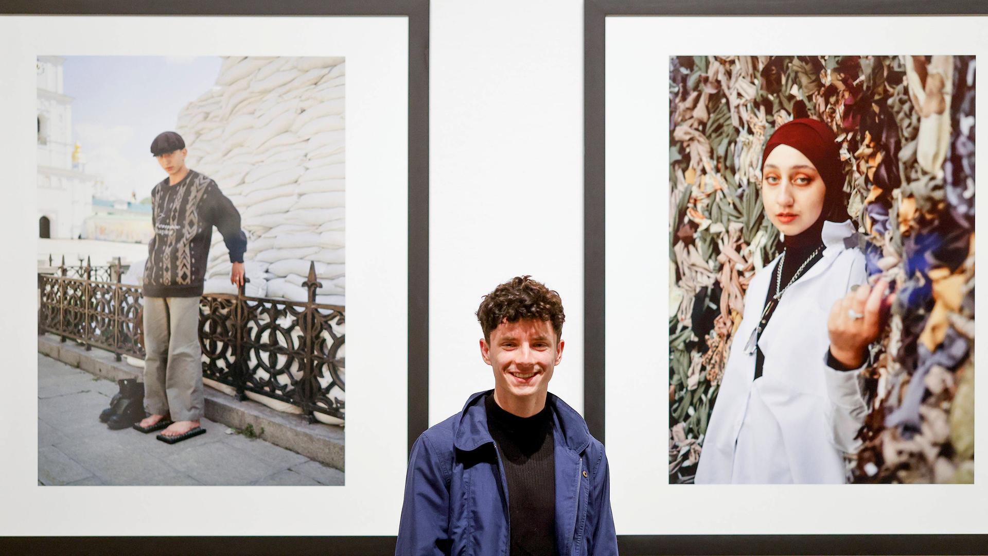 Sebastian Wells vor seinen preisgekrönten Fotoarbeiten "Young People Photographed in Kyiv, April and May 2022". Auf den Fotos sieht man rechts eine Frau mit Kopftuch, links einen Mann vor einer Mauer aus Sandsäcken. Sebastian Wells vor seinen preisgekrönten Fotoarbeiten "Young People Photographed in Kyiv, April and May 2022". Auf den Fotos sieht man rechts eine Frau mit Kopftuch, links einen Mann vor einer Mauer aus Sandsäcken.