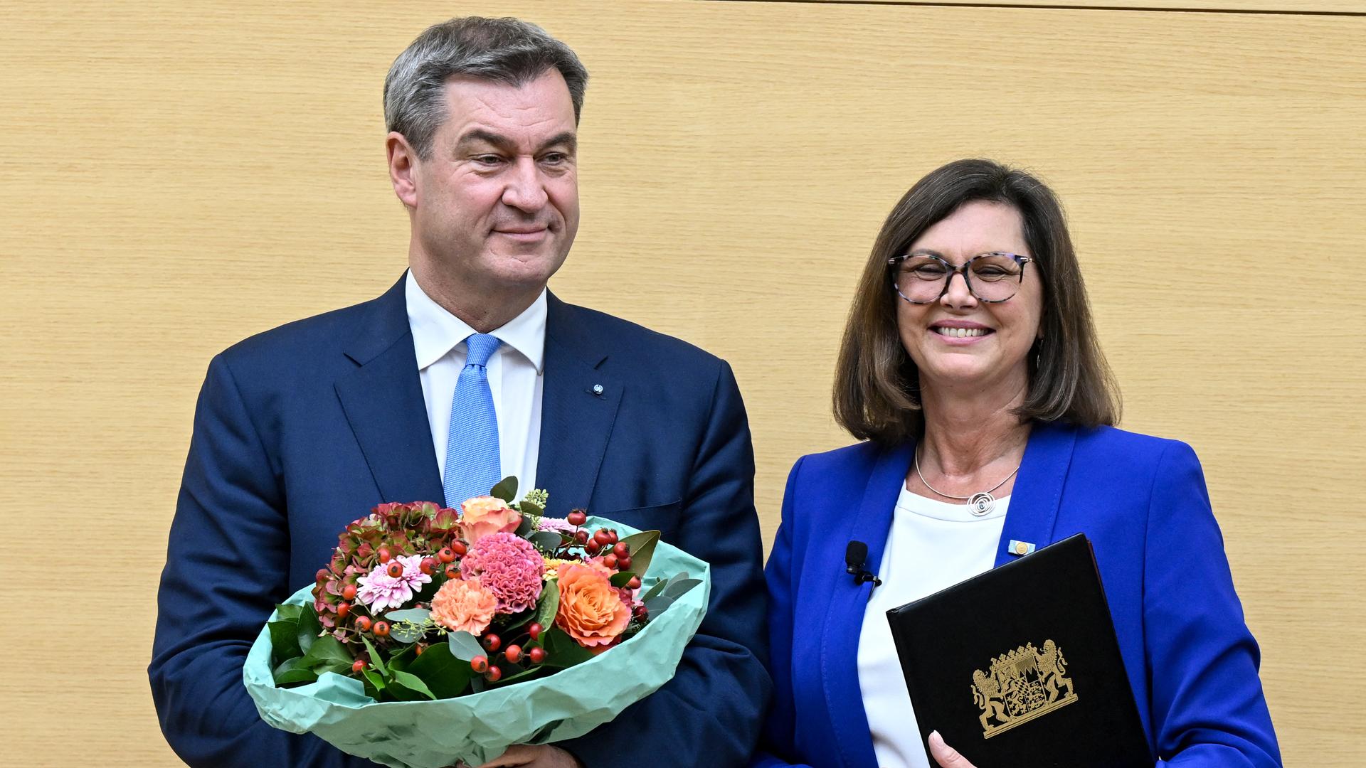 Der bayerische Ministerpräsident Markus Söder (links), und die Präsidentin des Bayerischen Landtags, Ilse Aigner stehen nebeneinander. Söder hält einen Blumenstrauß in Händen.