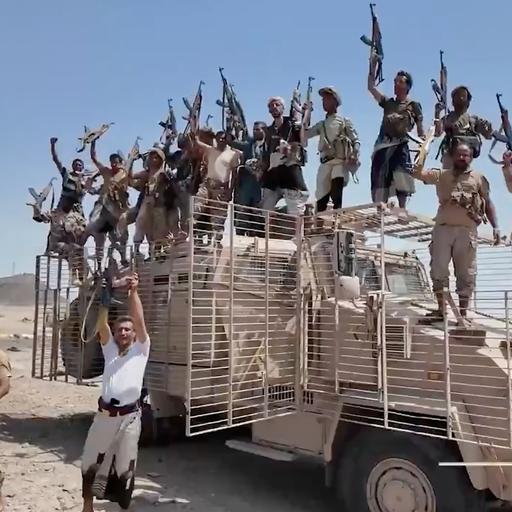 Huthi-Kämpfer stehen auf einem Militärfahrzeug. Sie halten ihre Gewehre in die Höhe.