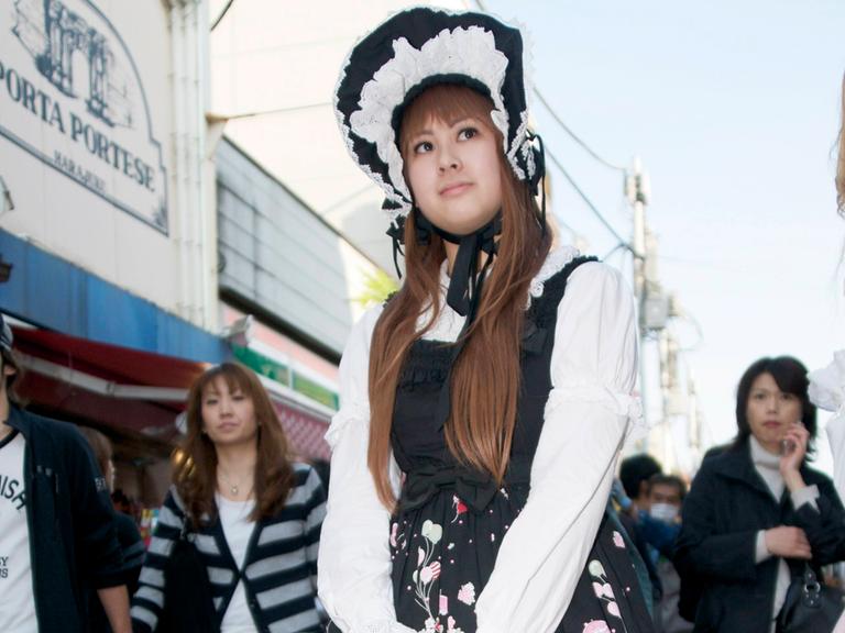 Eine junge Japanerin mit viktorianischem Spitzenhäubchen, Rüschenbluse in weiß und weiten Röcken in schwarz-rosa