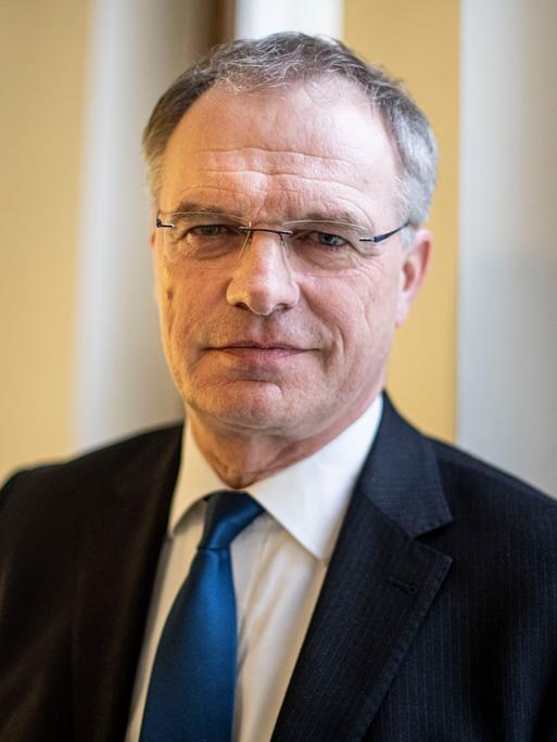 Stefan Raue schaut in die Kamera. Er trägt einen schwarzen Anzug mit dunkelblauer Krawatte und eine eckige, randlose Brille.