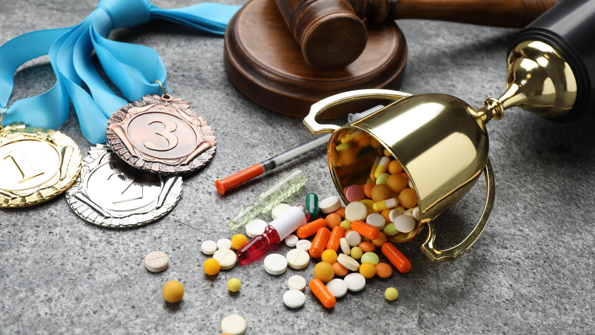 Medaillen, ein Pokal und verschiedene Pillen liegen auf einer Oberfläche.