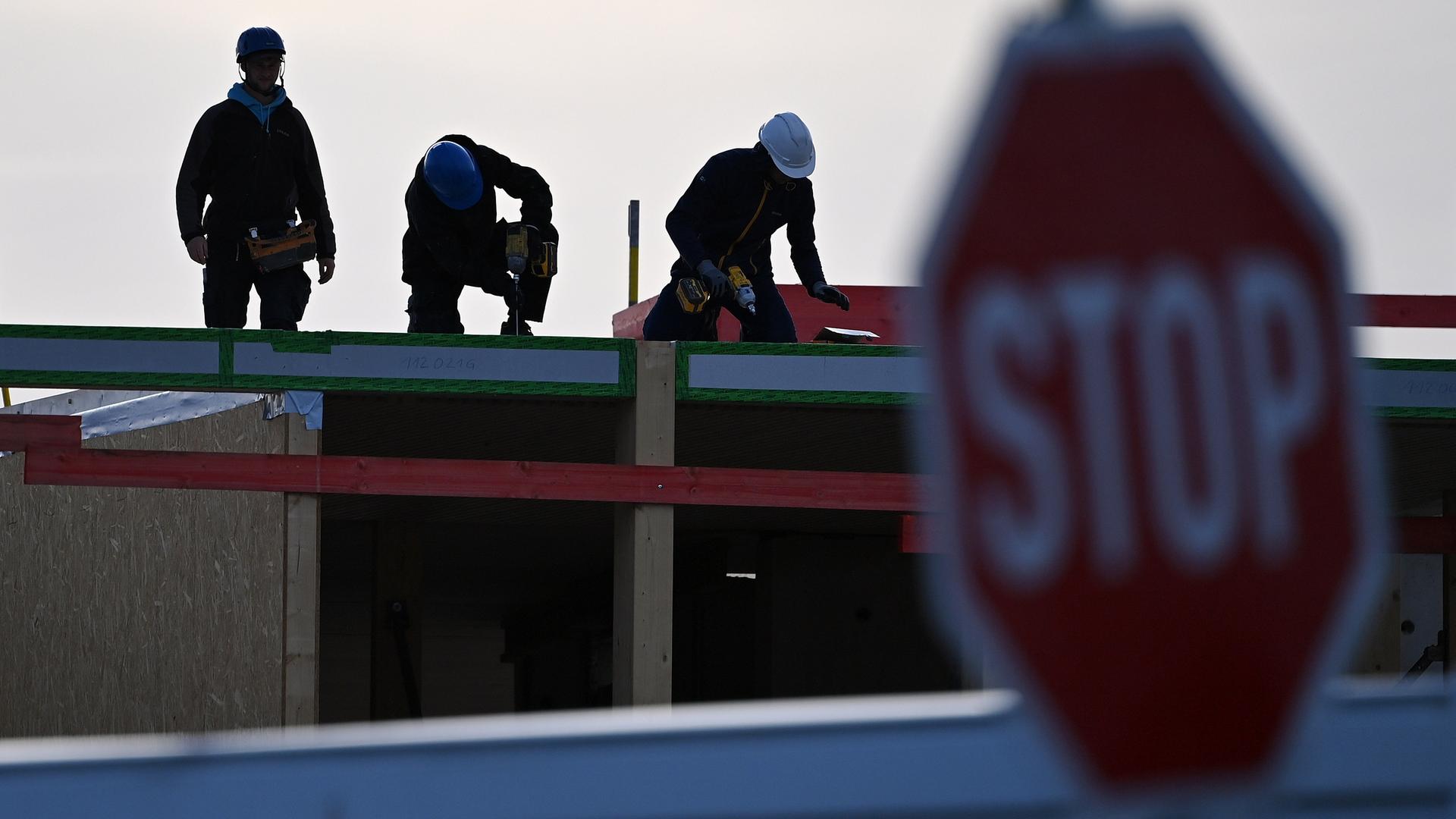 Eine Baustelle mit Arbeiter, die Helm tragen, im Vordergrund ist ein Stopp-Schild.
