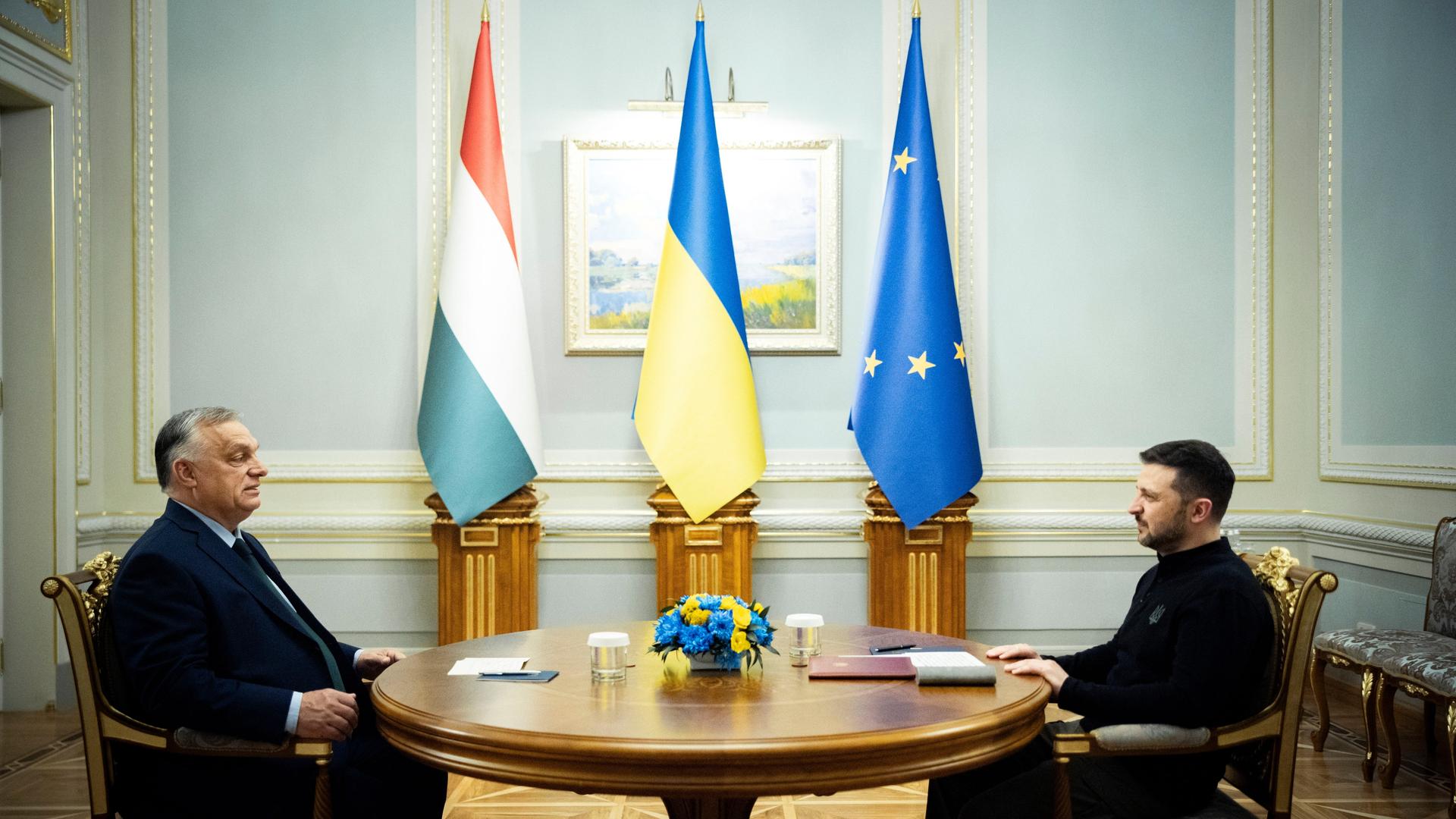 Der ukrainische Präsident Wolodymyr Selenskyj (r) und der ungarische Ministerpräsident Viktor Orban sitzen sich an einem Tisch gegenüber. Hinter ihnen sind die Flaggen, Ungarns, der Ukraine und Europas. 