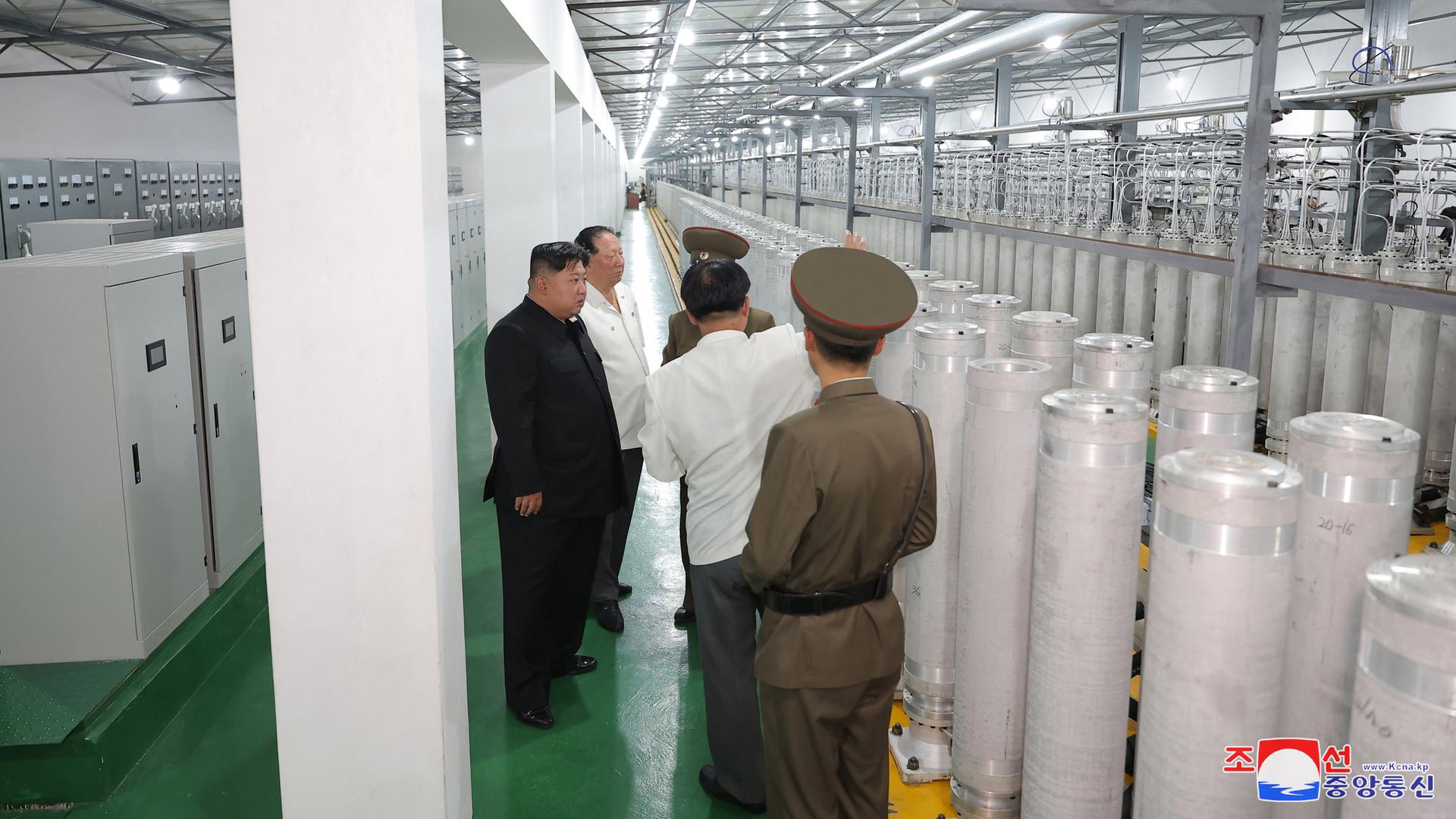 Das Bild zeigt Kim Jon Un mit Militärs und Wissenschaftlern in einer großen Halle mit langen Reihen und Maschinen, die eine Urananreicherungsanlage darstellen soll.