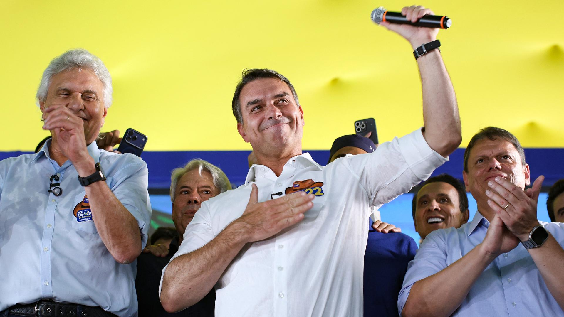 Der brasilianische Politiker Flávio Bolsonaro hält die rechte Hand vor die Brust, in der linken Hand hält er ein Mikrofon.