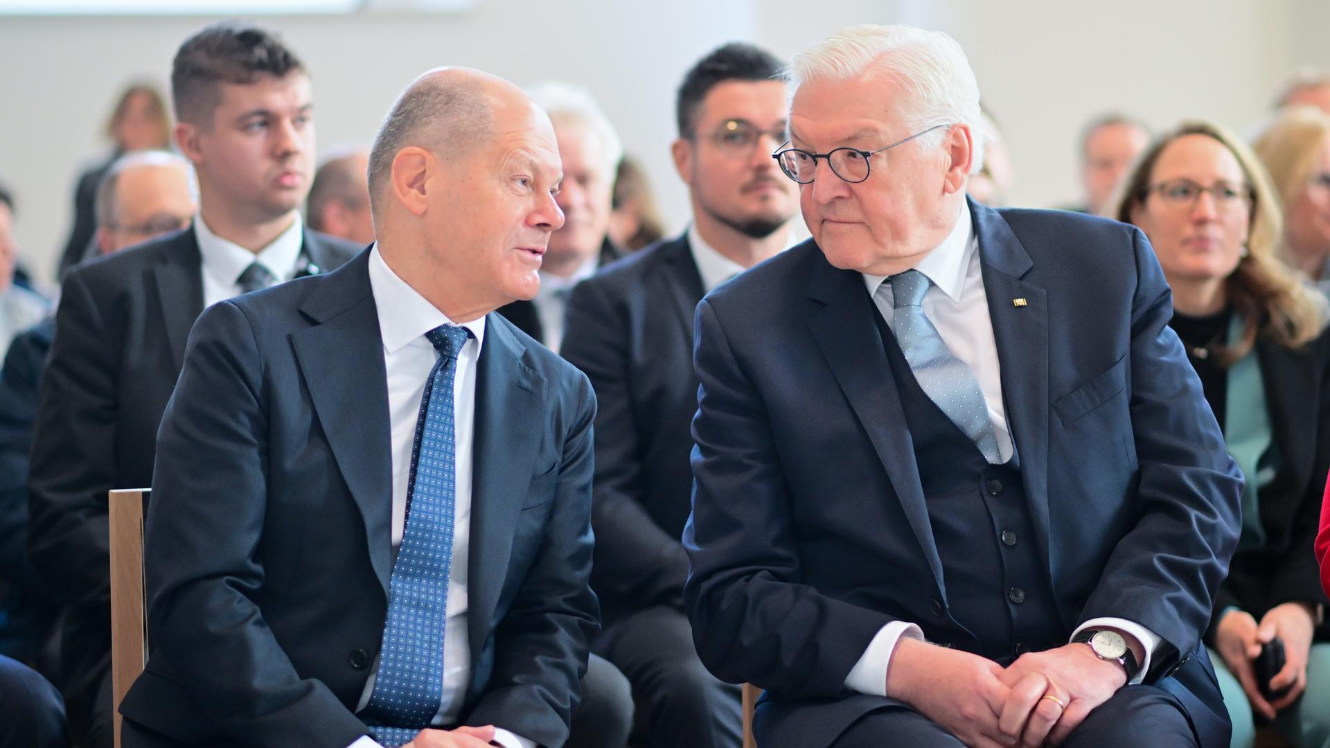 Bundeskanzler Olaf Scholz (SPD,l) und Bundespräsident Frank-Walter Steinmeier sitzen leicht zueinander geneigt auf Stühlen und sprechen miteinander. 