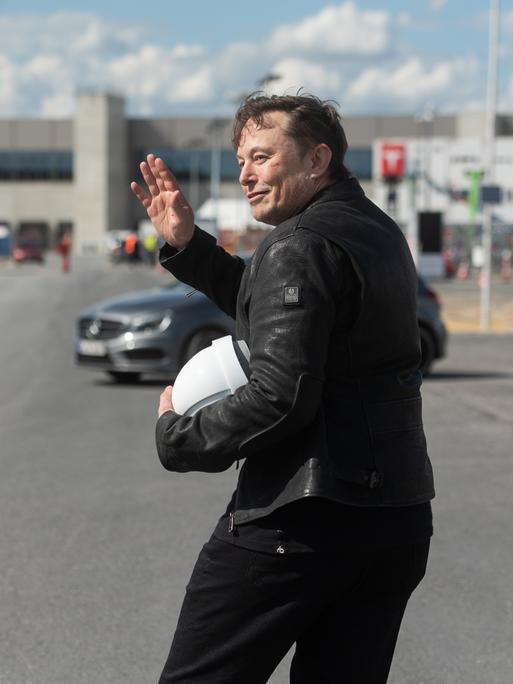 Tesla-Chef Elon Musk mit einem Baustellenhelm in der Hand steht vor der Tesla-Fabrik in Grünheide