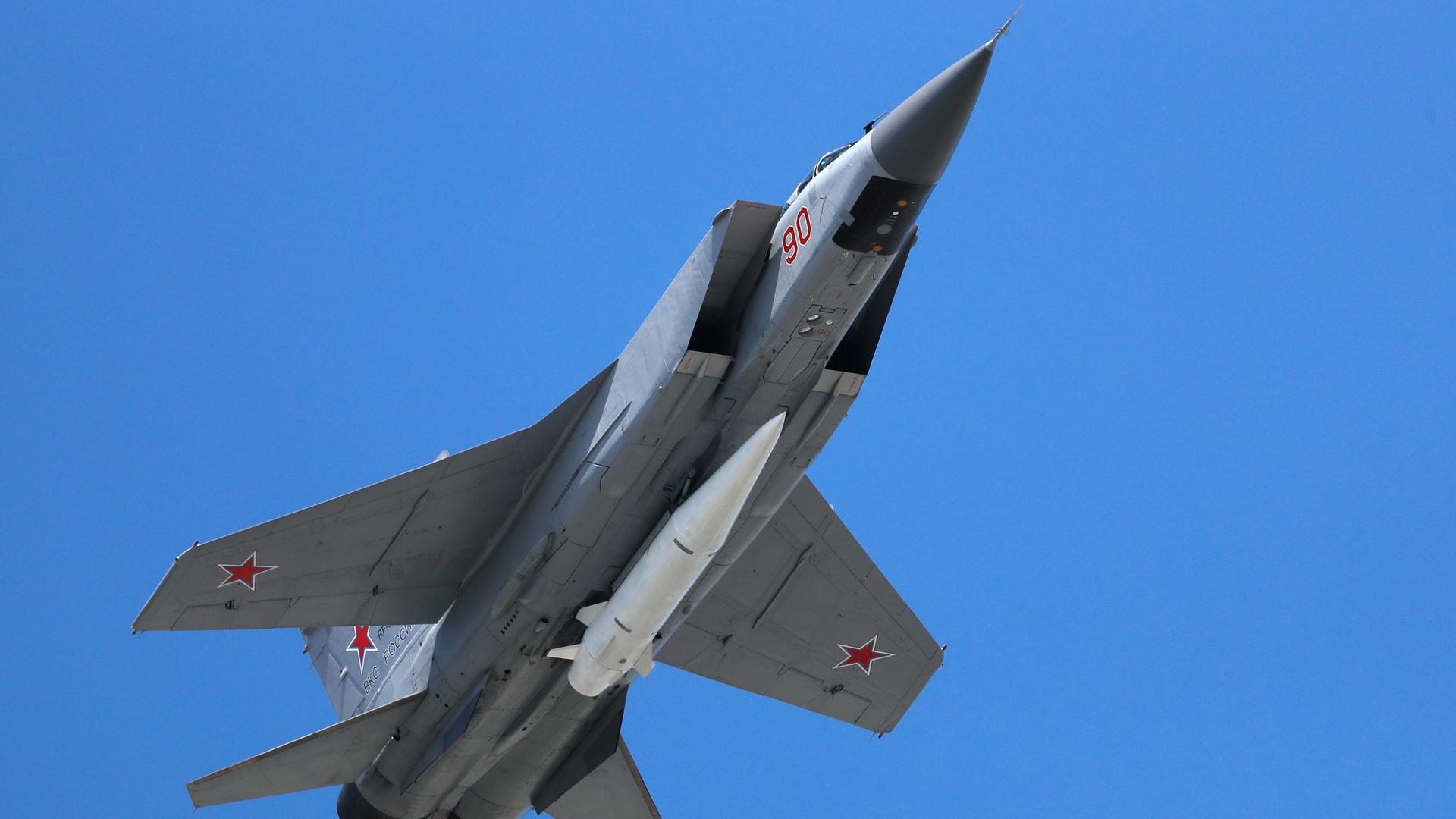 Ein russisches Militärflugzeug in der Luft. Am Rumpf ist eine weiße Rakete befestigt.