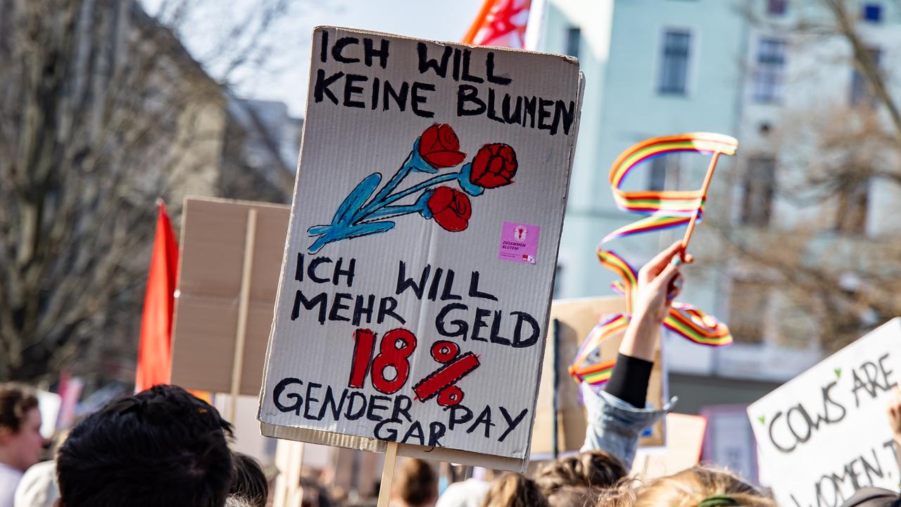 Ein Schild mit der Aufschrift "Ich will keine Blumen, ich will mehr Geld. 18% Gender Pay Gap" ist auf einer Demonstration in Berlin zu sehen.