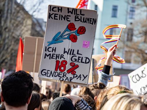 Ein Schild mit der Aufschrift "Ich will keine Blumen, ich will mehr Geld. 18% Gender Pay Gap" ist auf einer Demonstration in Berlin zu sehen.
