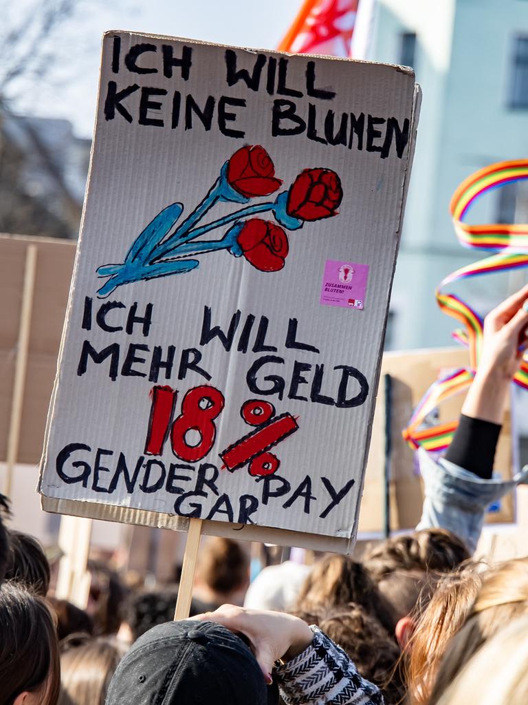 Ein Schild mit der Aufschrift "Ich will keine Blumen, ich will mehr Geld. 18% Gender Pay Gap" ist auf einer Demonstration in Berlin zu sehen.