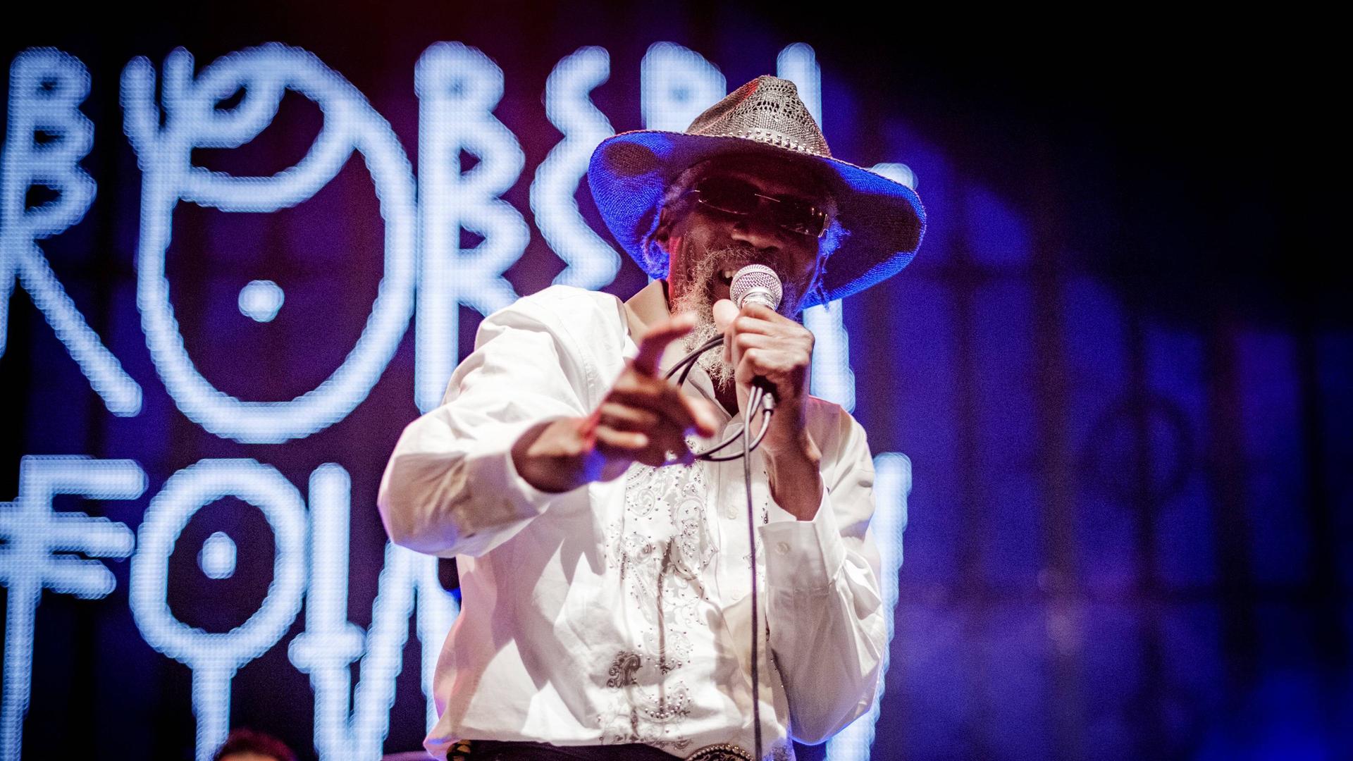 Robert Finley steht 2018 auf einer Bühne des Musicas do Mundo Festivals mit Hut und dunkler Brille. 