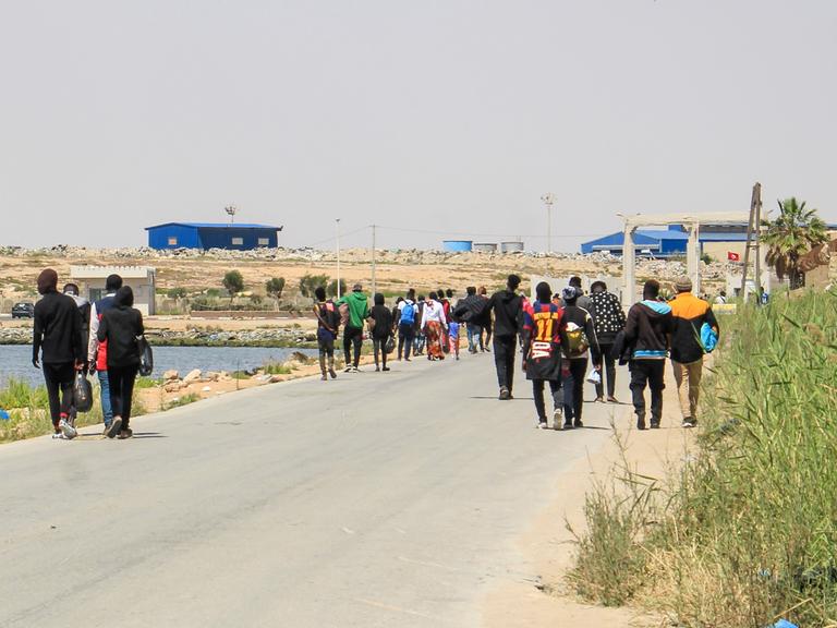 Migranten, die von tunesischen Einsatzkräften auf dem Meer aufgespürt wurden, gehen eine Strasse hinunter, nachdem sie am Hafen zurück an Land gelassen wurden.