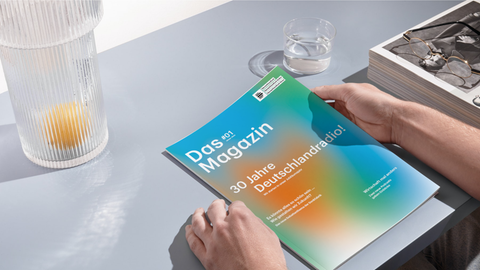 Das Deutschlandradio-Magazin, Ausgabe Januar 2024 liegt auf einem grauen Tisch, man sieht zwei männliche Hände, die es halten.