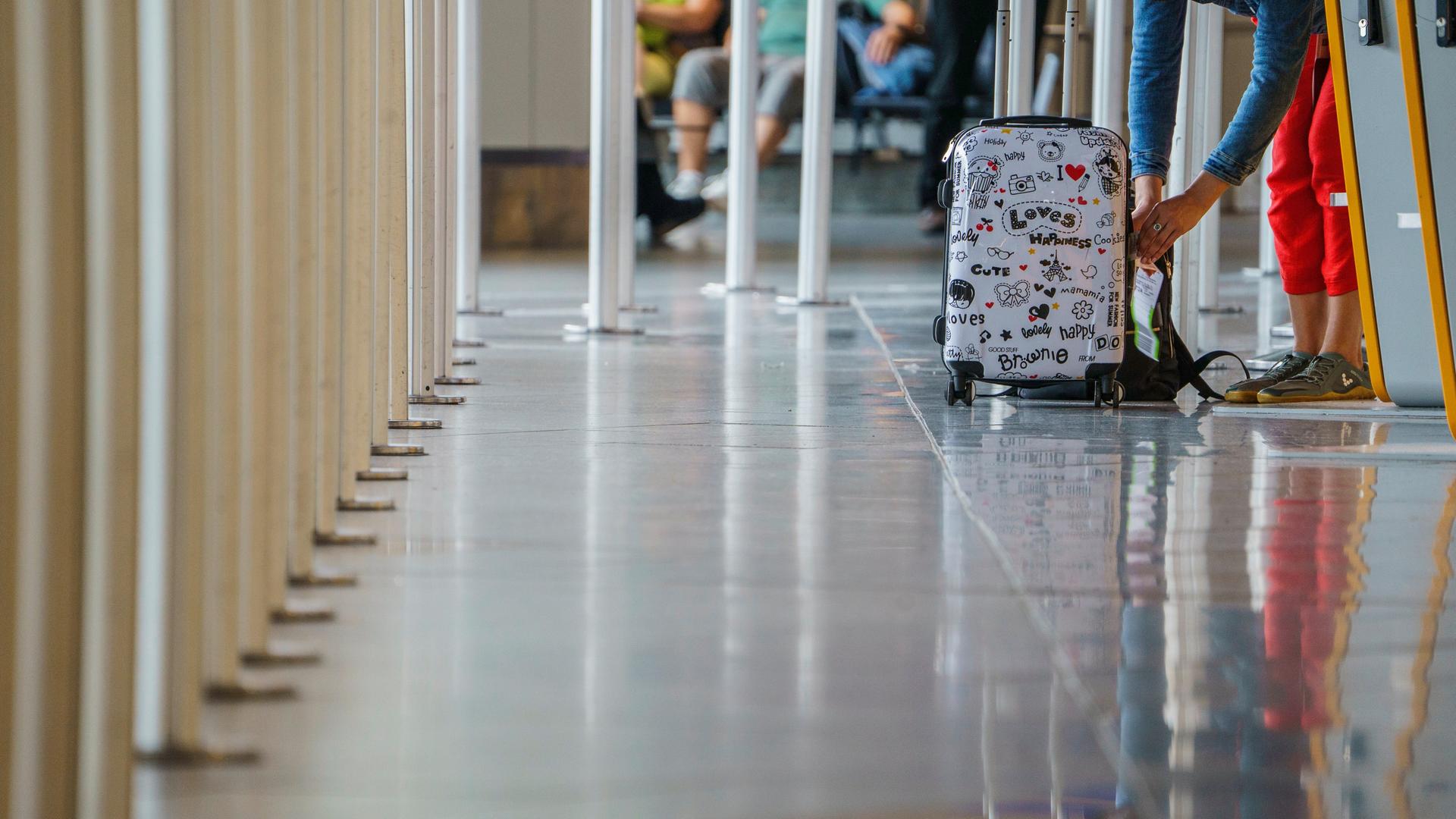 Eine Frau bringt im Terminal 1 des Rhein-Mainflughafen den Strichcode-Aufkleber an ihrem Koffer an.