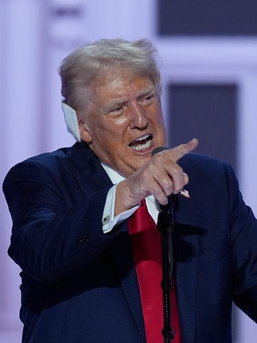 Donald Trump steht beim Parteitag der Republikaner in Milwaukee auf der Bühne, hebt den Zeigefinger und hat ein Pflaster ans Ohr geklebt.