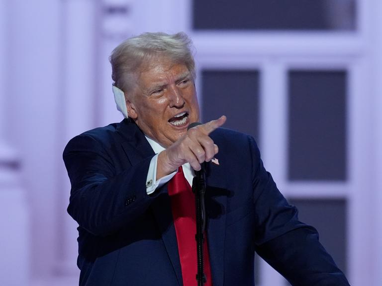 Donald Trump steht beim Parteitag der Republikaner in Milwaukee auf der Bühne, hebt den Zeigefinger und hat ein Pflaster ans Ohr geklebt.