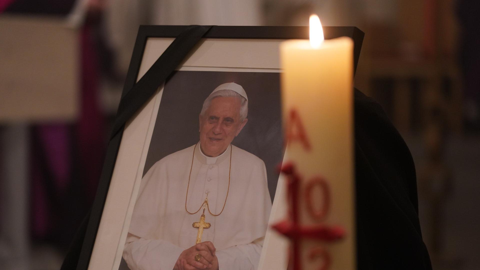 Ein Foto des gestorbenen Papstes Benedikt XVI. mit einer brennenden Kerze daneben. 