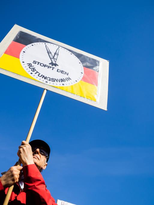 Ein Mann hält beim Ostermarsch des "Netzwerks Friedenskooperative" unter dem Motto "Die Waffen nieder!" am Oranienplatz in Berlin-Kreuzberg ein Schild mit der Aufschrift "Stoppt den Rüstungswahn". Ebenfalls stellt es eine "Raketen-Uhr" dar, die auf fünf vor zwölf steht.