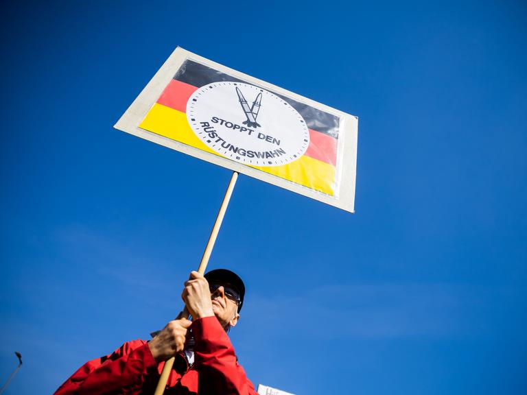 Ein Mann hält beim Ostermarsch des "Netzwerks Friedenskooperative" unter dem Motto "Die Waffen nieder!" am Oranienplatz in Berlin-Kreuzberg ein Schild mit der Aufschrift "Stoppt den Rüstungswahn". Ebenfalls stellt es eine "Raketen-Uhr" dar, die auf fünf vor zwölf steht.