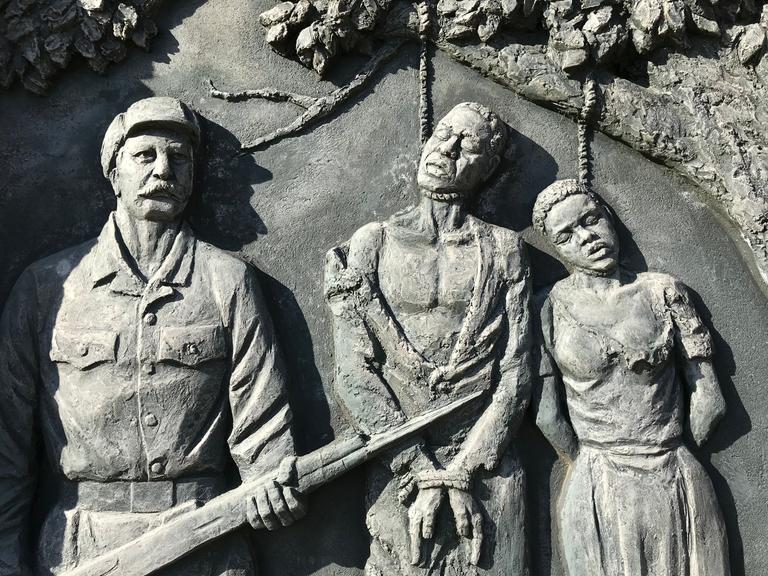Ein Denkmal zeigt drei an einem Baum gehenkte Menschen und zwei bewaffnete Soldaten neben ihnen.