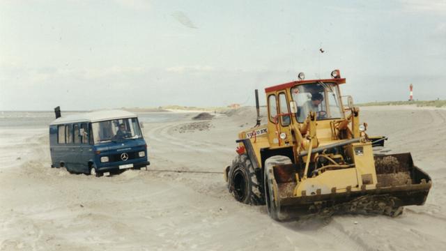Ein Ü-Wagen vom Deutschlandfunk steckt im Sand am Strand von Wangerooge fest und wird von einem Bagger herausgezogen (1985)