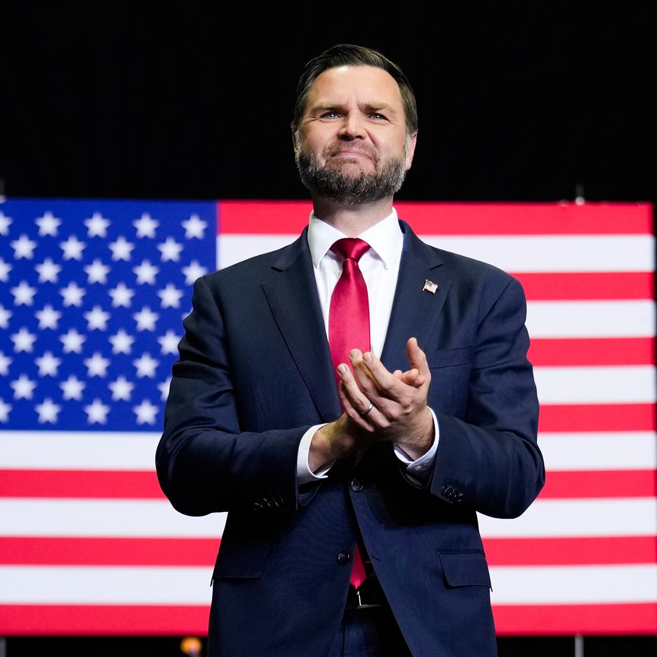 US-Vizepräsident JD Vance steht vor einer Flagge der Vereinigten Staaten und applaudiert.