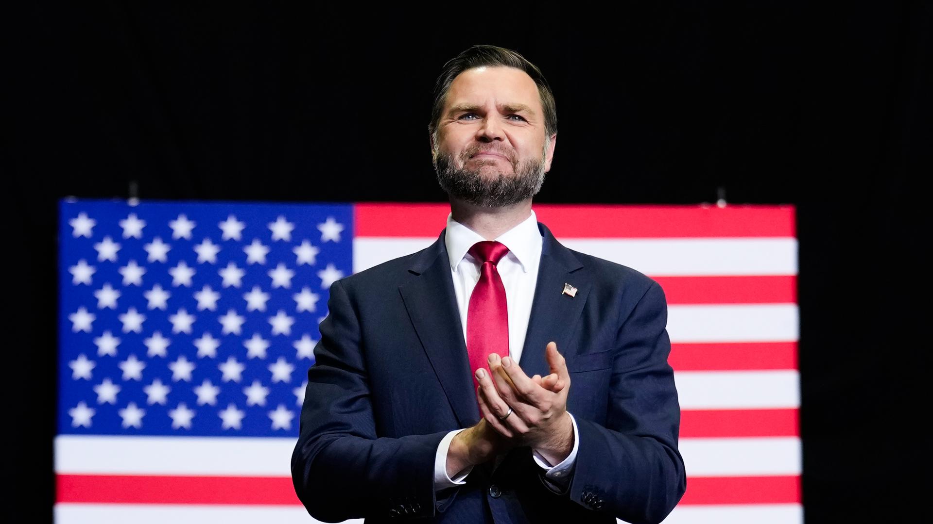 US-Vizepräsident JD Vance steht vor einer Flagge der Vereinigten Staaten und applaudiert.
