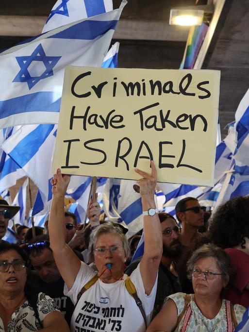 Israelische Demonstranten halten israelkische Fahnen und Plakate während einer Protestaktion. Auf einem Plakat ist auf englisch zu lesen: Kriminelle haben Israel übernommen. Israelische Demonstranten halten israelkische Fahnen und Plakate während einer Protestaktion. Auf einem Plakat ist auf englisch zu lesen: Kriminelle haben Israel übernommen.