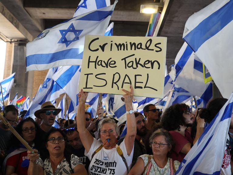 Israelische Demonstranten halten israelkische Fahnen und Plakate während einer Protestaktion. Auf einem Plakat ist auf englisch zu lesen: Kriminelle haben Israel übernommen. Israelische Demonstranten halten israelkische Fahnen und Plakate während einer Protestaktion. Auf einem Plakat ist auf englisch zu lesen: Kriminelle haben Israel übernommen.