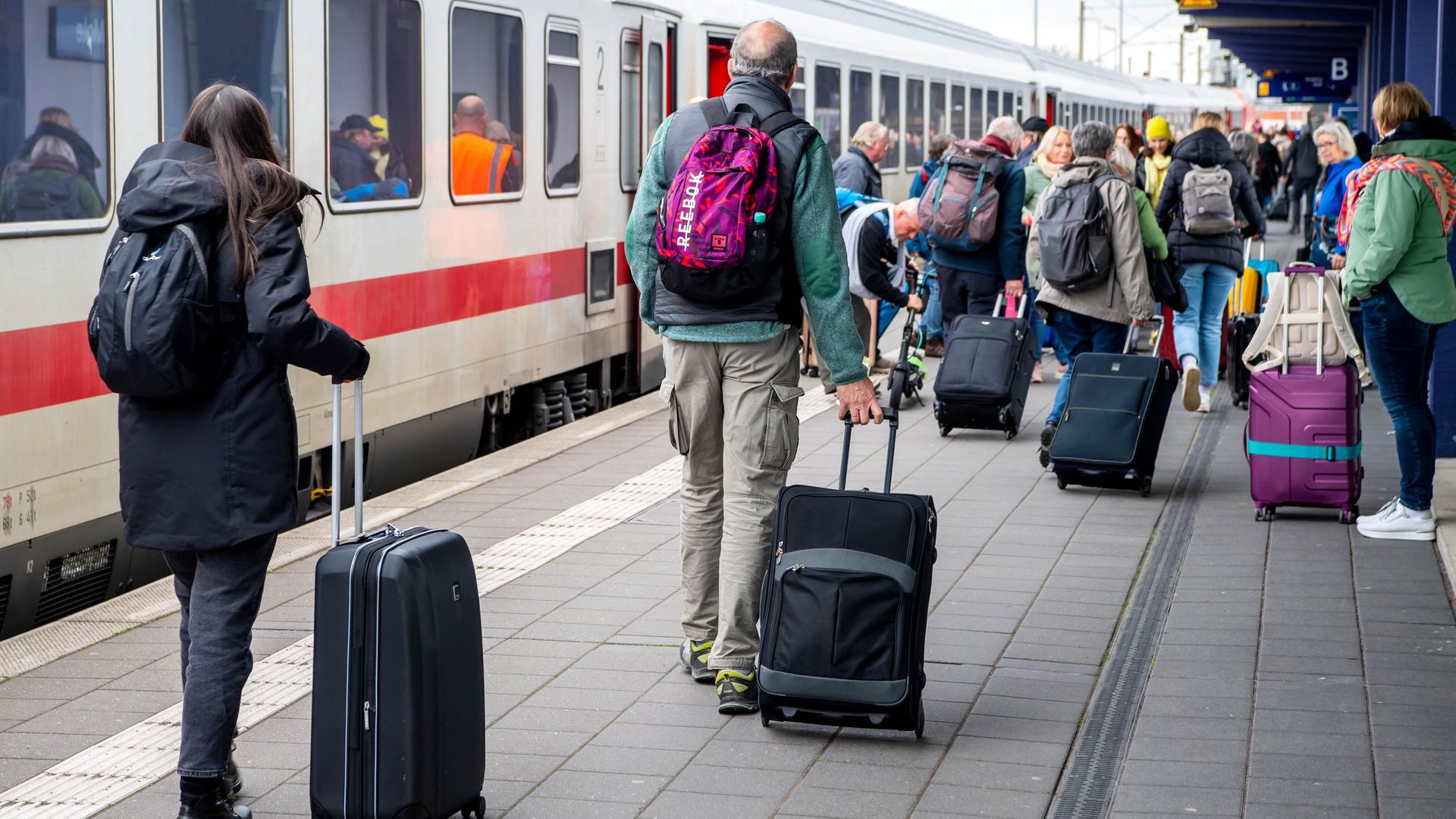 Reisende mit Koffern gehen an einem IC am Bahnhof Norddeich-Mole entlang.
