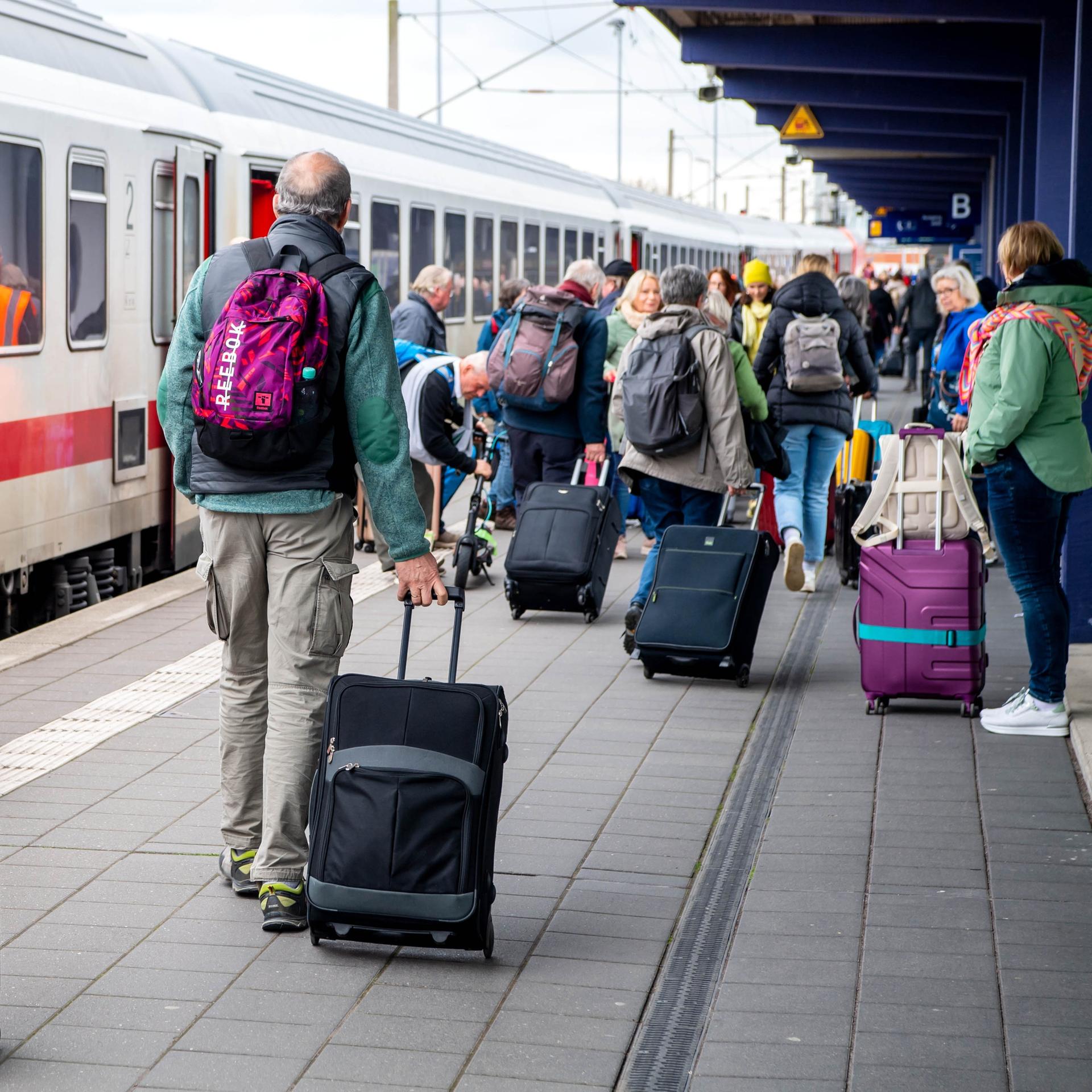 Reisende mit Koffern gehen an einem IC am Bahnhof Norddeich-Mole entlang.