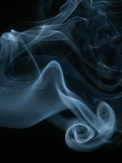 Rauch einer Zigarette steigt gegen schwarzen Hintergrund auf