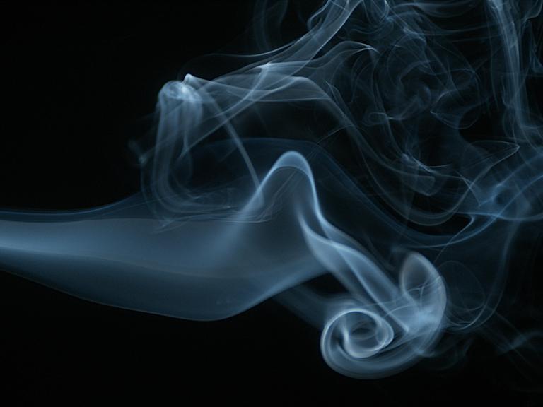 Rauch einer Zigarette steigt gegen schwarzen Hintergrund auf