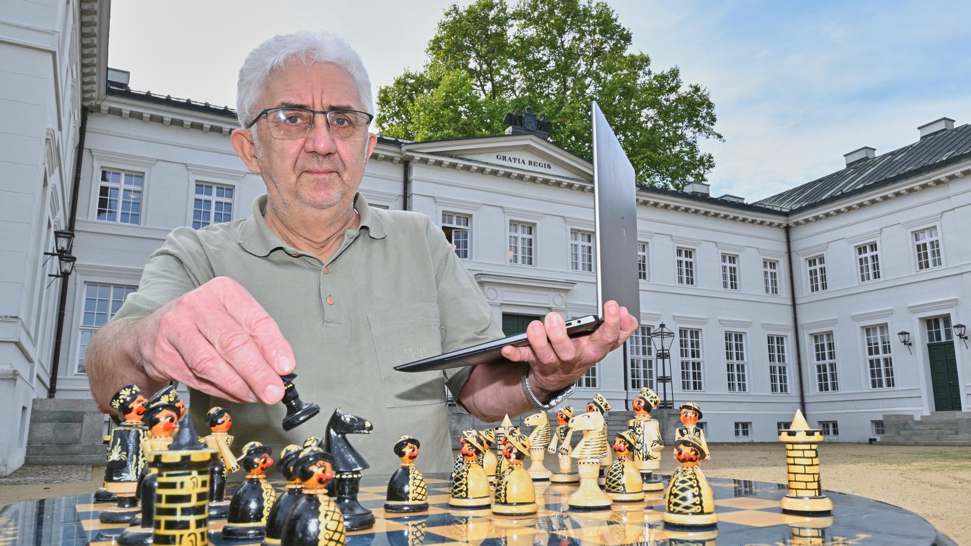 Manfred Scheiba, Präsident vom Deutschen Fernschachbund (BdF), sitzt mit seinem Laptop und einem Schachspiel vor dem Schloss Neuhardenberg. Hier findet der internationale Fernschachkongress statt.