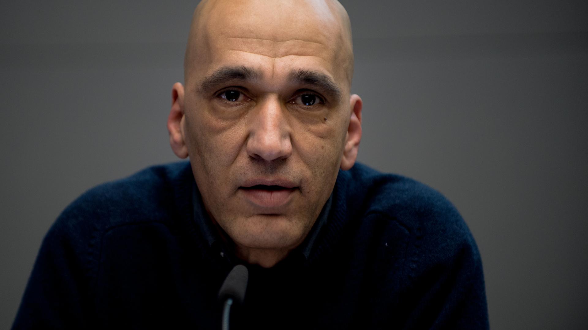 Nahaufnahme von Tahir Della vor einem kleinen schwarzen Mikrofon. Nahaufnahme von Tahir Della vor einem kleinen schwarzen Mikrofon.