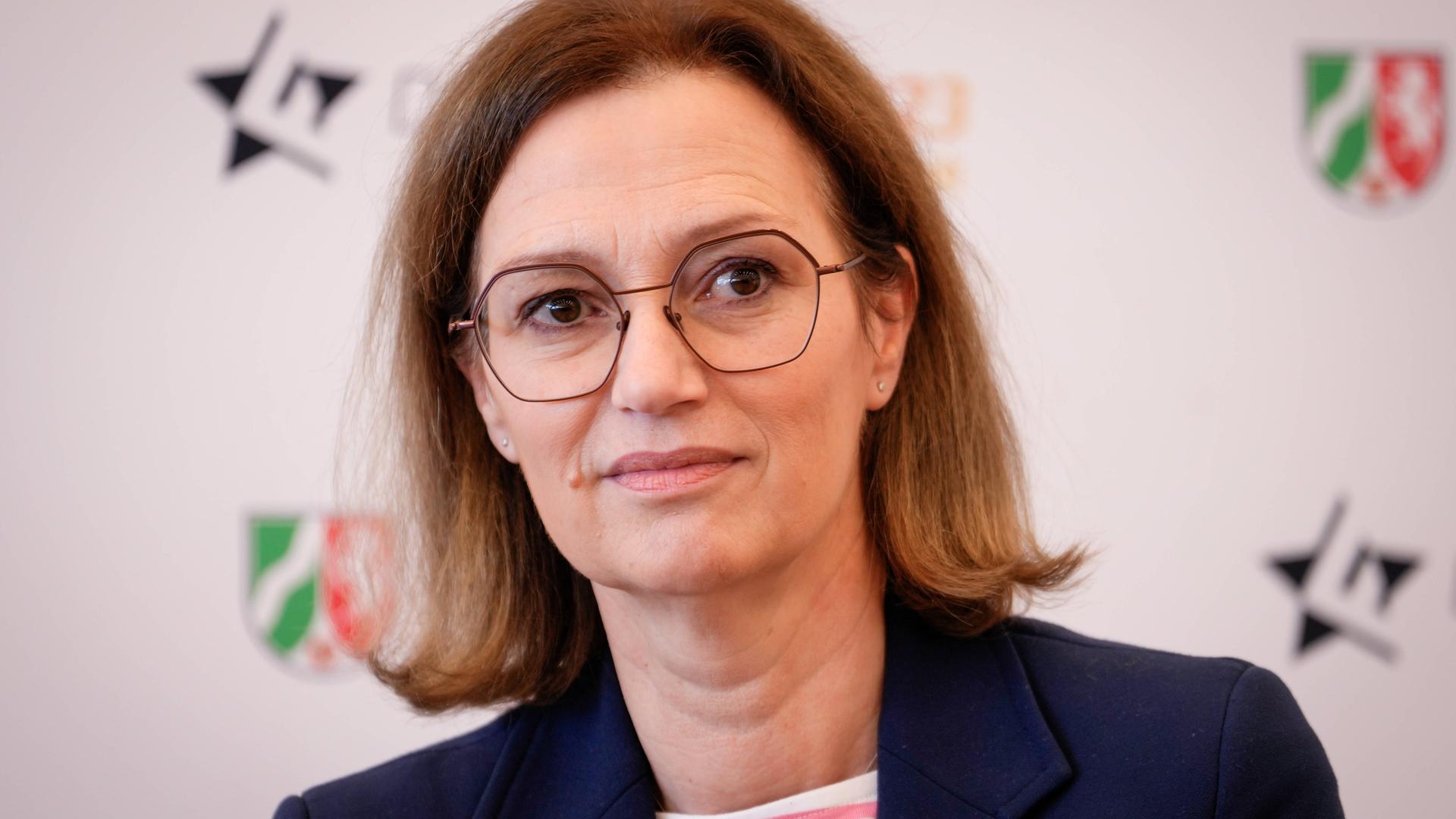 Bettina Schausten bei einer Pressekonferenz, mit Brille und dunkelblauer Jacke.