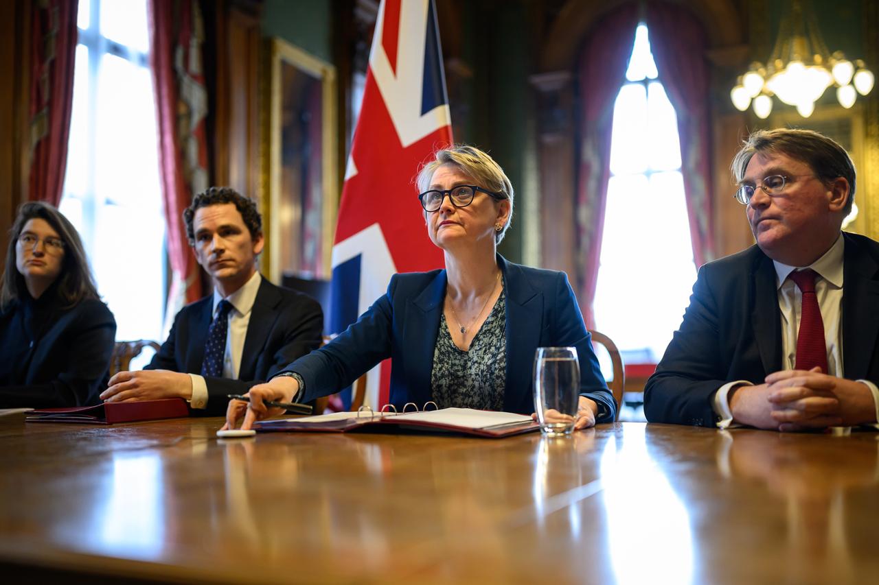 Die britische Außenministerin Yvette Cooper sitzt neben mehreren Personen an einem Schreibtisch. 