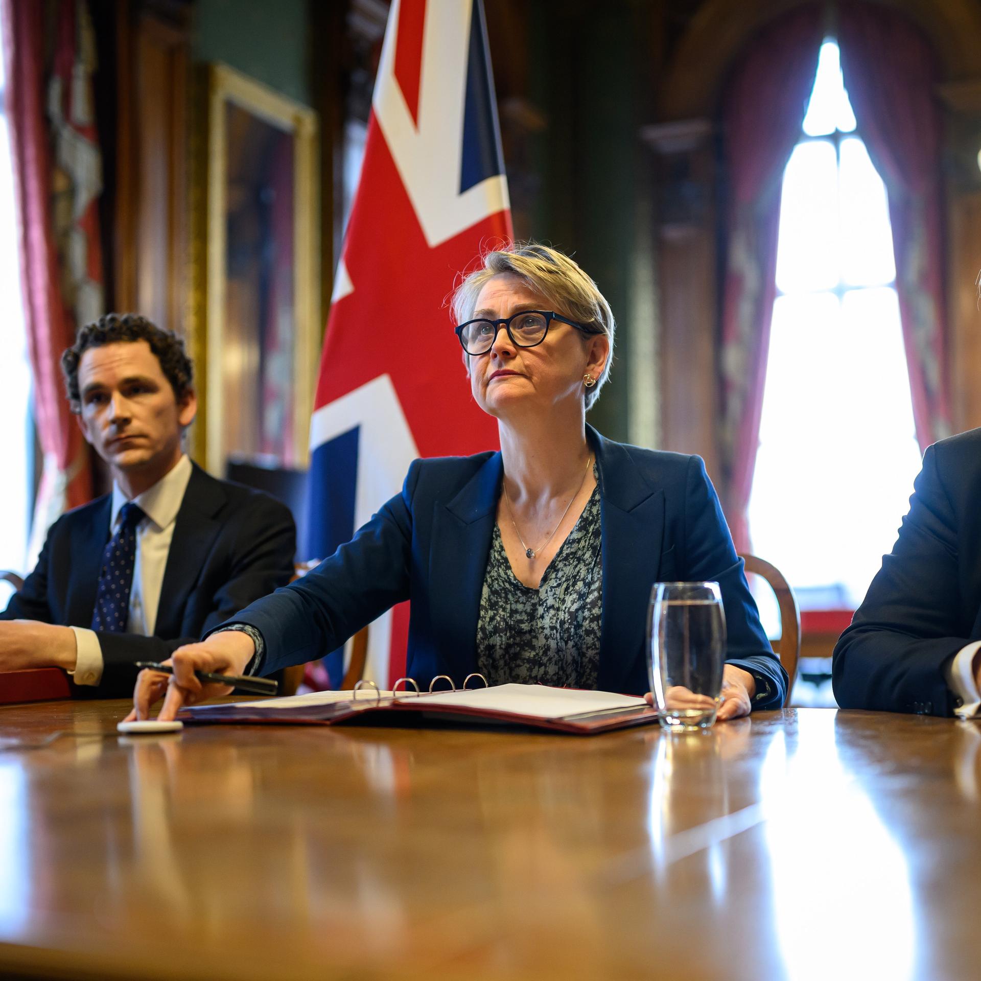 Die britische Außenministerin Yvette Cooper sitzt neben mehreren Personen an einem Schreibtisch. 