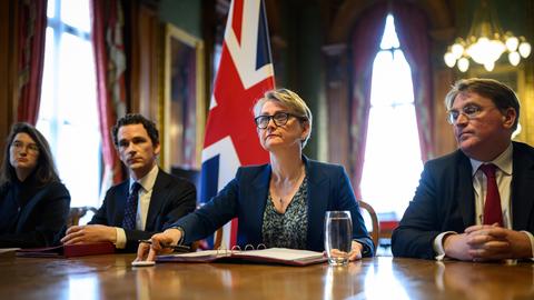 Die britische Außenministerin Yvette Cooper sitzt neben mehreren Personen an einem Schreibtisch. 