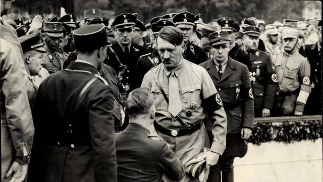 Schwarz-Weiß-Fotografie: Auf dem Nürnberger Reichsparteitag ist Adolf Hitler im Gespräch mit einem Veteranen, daneben Männer von der SS und SA