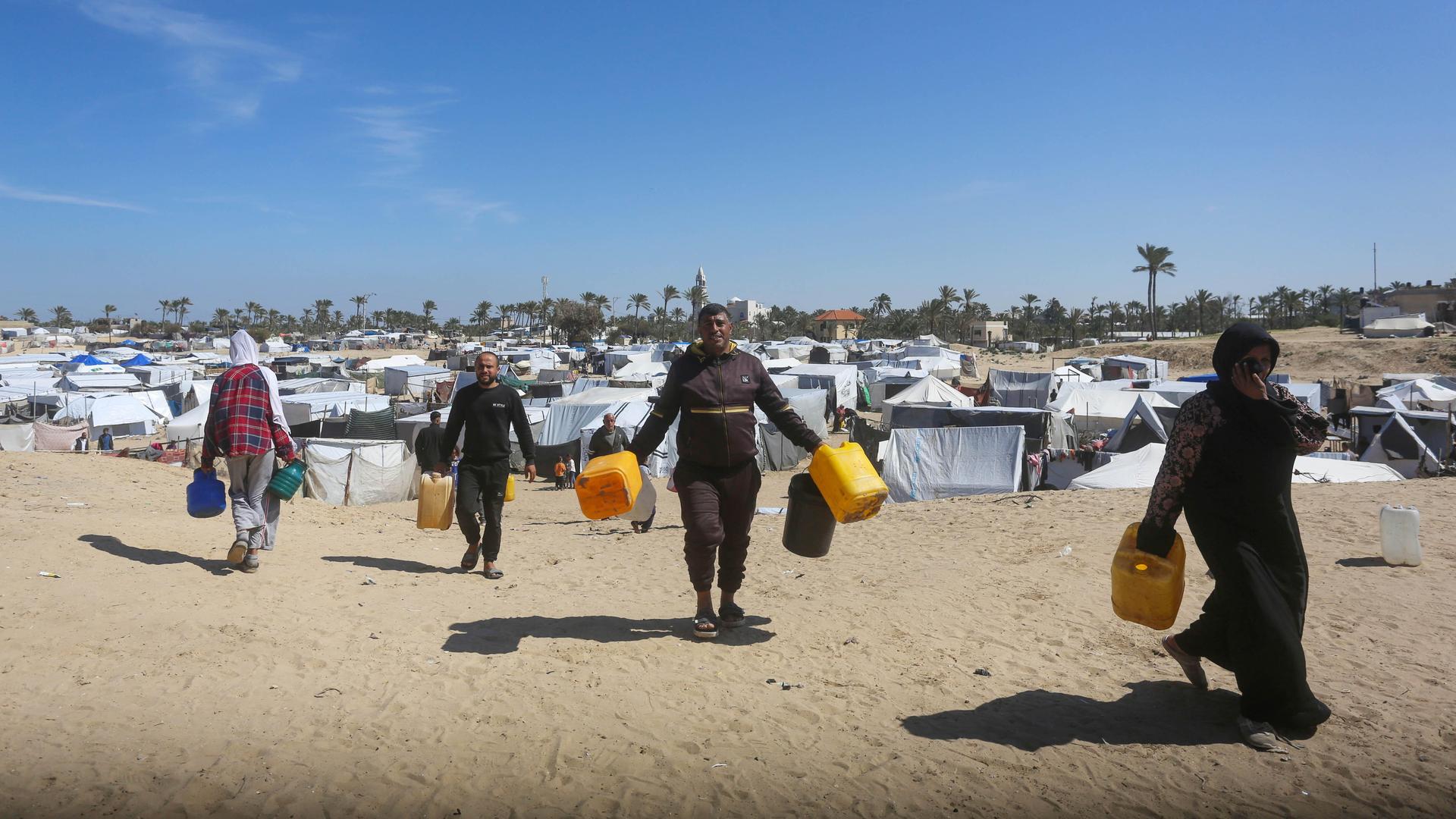 Männer und Frauen tragen gelbe Wasserkanister in einem Flüchtlingslager.