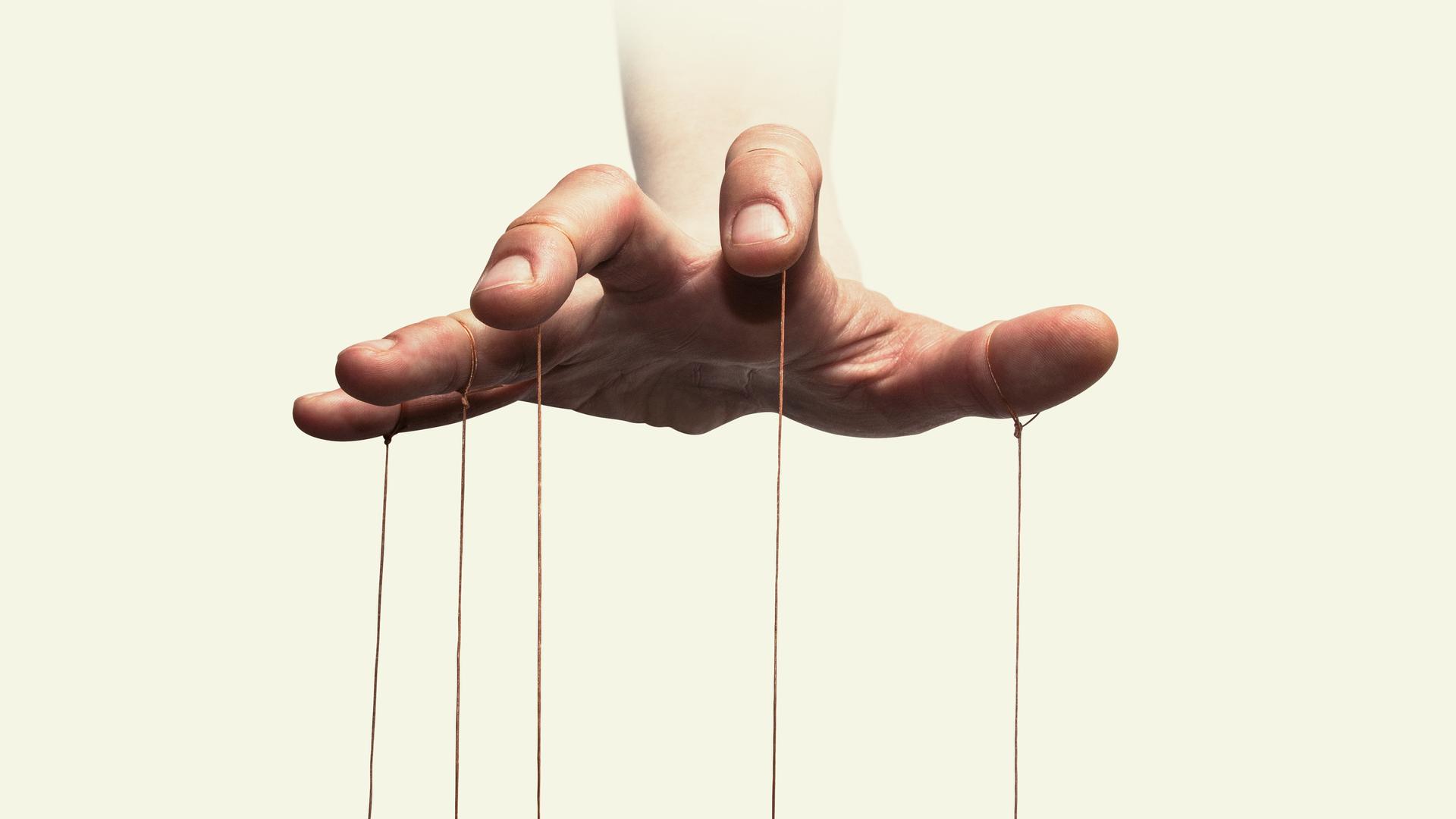 Nahaufnahme der Hand eines Puppenspielers mit an den einzelnen Fingern befestigten Fäden.