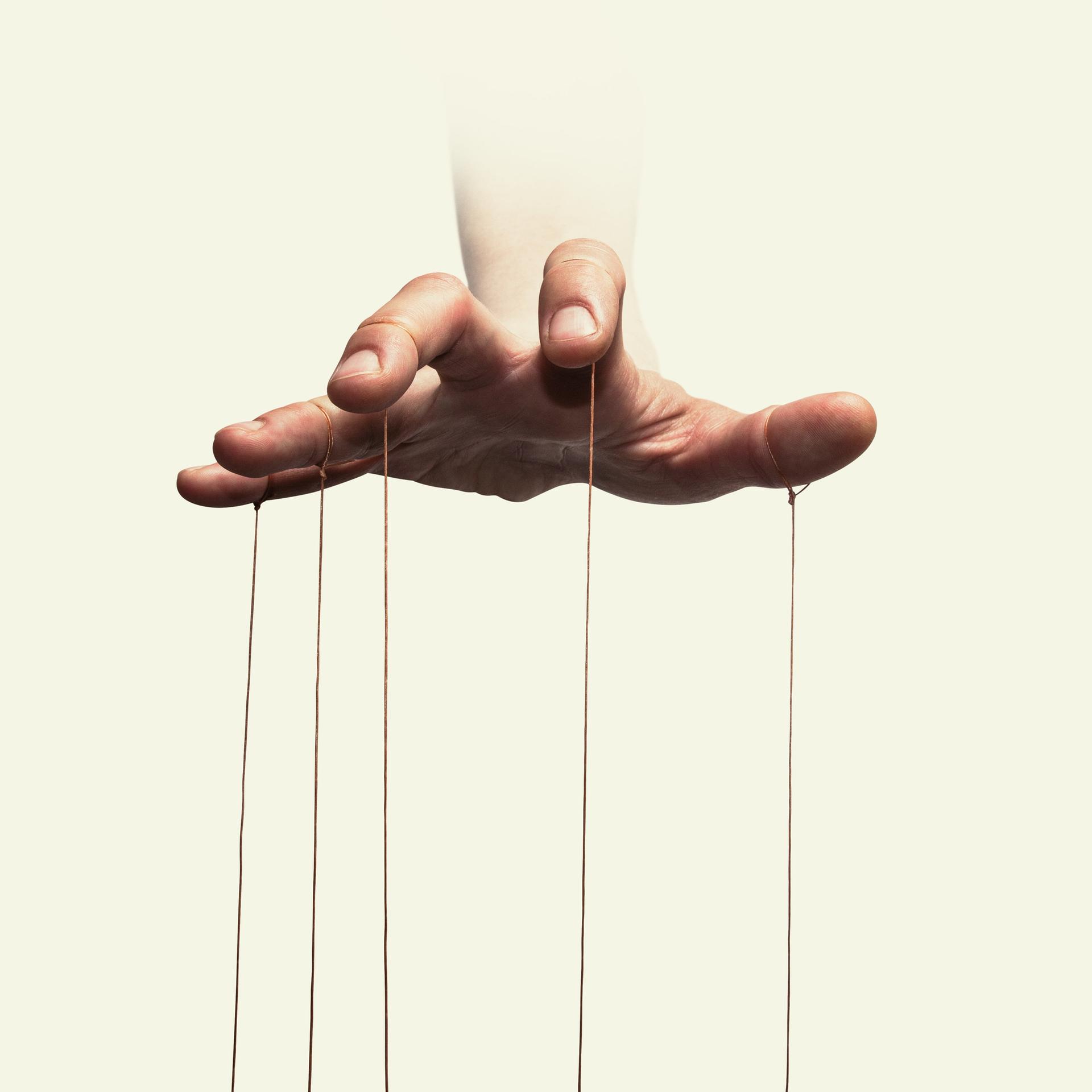 Nahaufnahme der Hand eines Puppenspielers mit an den einzelnen Fingern befestigten Fäden.