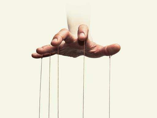 Nahaufnahme der Hand eines Puppenspielers mit an den einzelnen Fingern befestigten Fäden.