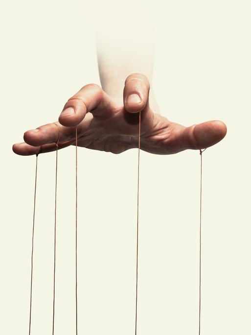 Nahaufnahme der Hand eines Puppenspielers mit an den einzelnen Fingern befestigten Fäden.
