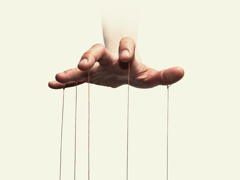 Nahaufnahme der Hand eines Puppenspielers mit an den einzelnen Fingern befestigten Fäden.