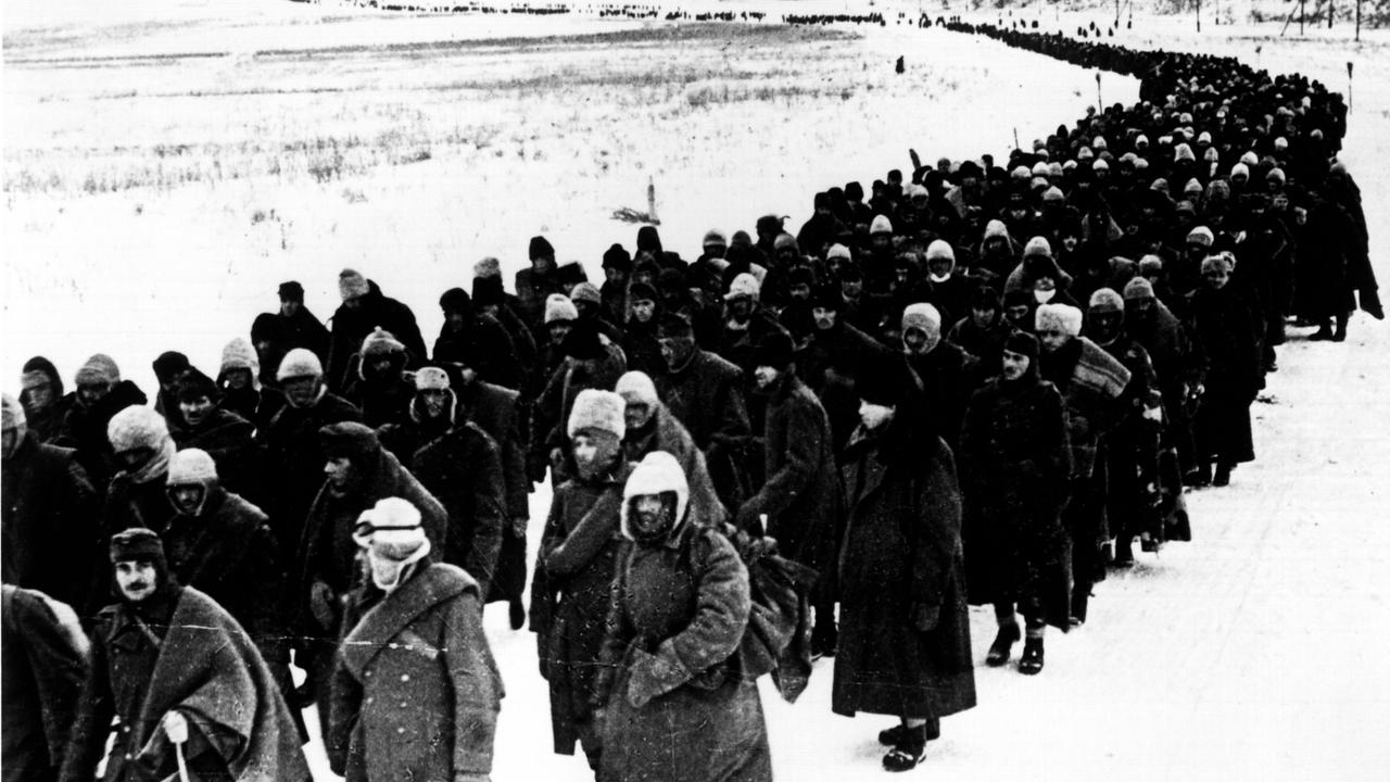 Auf dem groben schwarz-weißen Foto sieht man eine Kolonne zerlumpter Gefangener, die sich bis zum Horizont zieht. Sie geht durch eine flache Schneelandschaft.