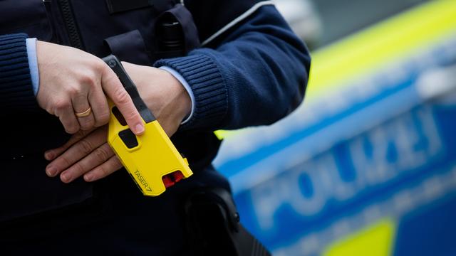 Ein Polizist hat einen Taser in der Hand.